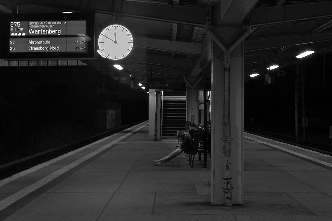 A lone young woman waits for her train on a deserted platform.