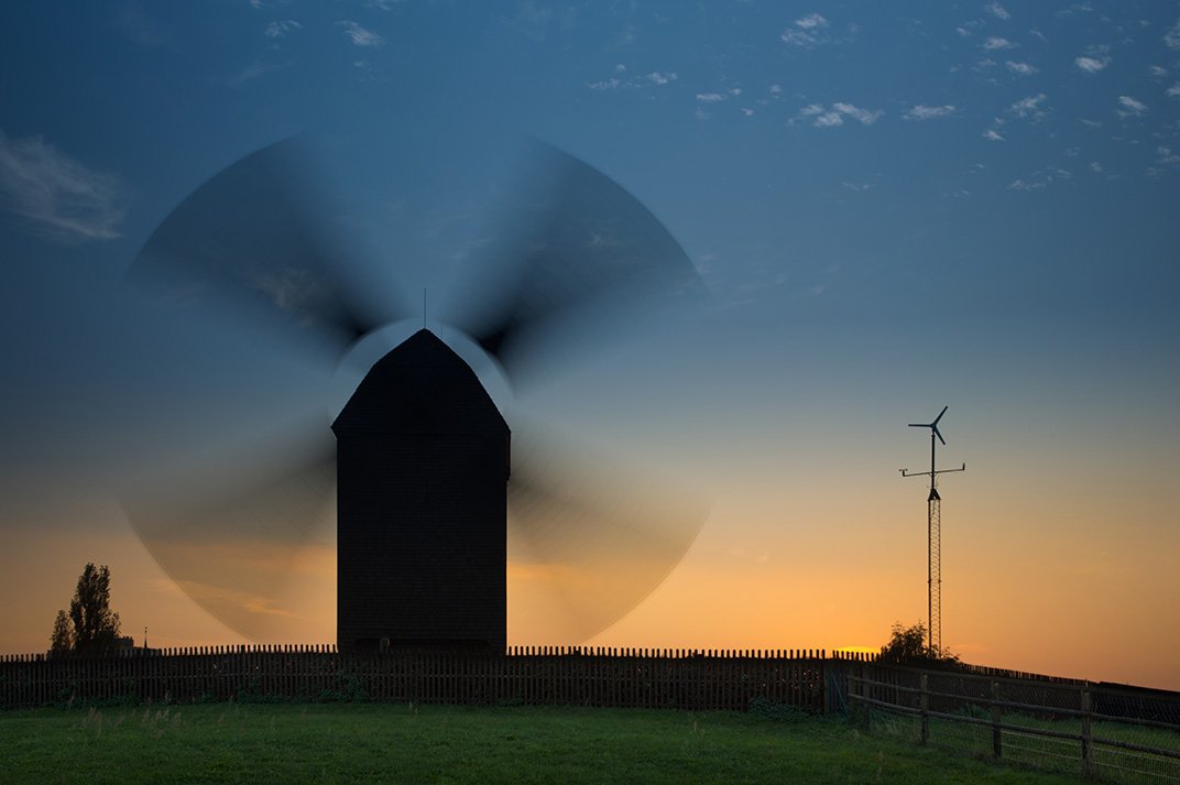 The sun sets behind the windmill in Alt-Marzahn as it turns.